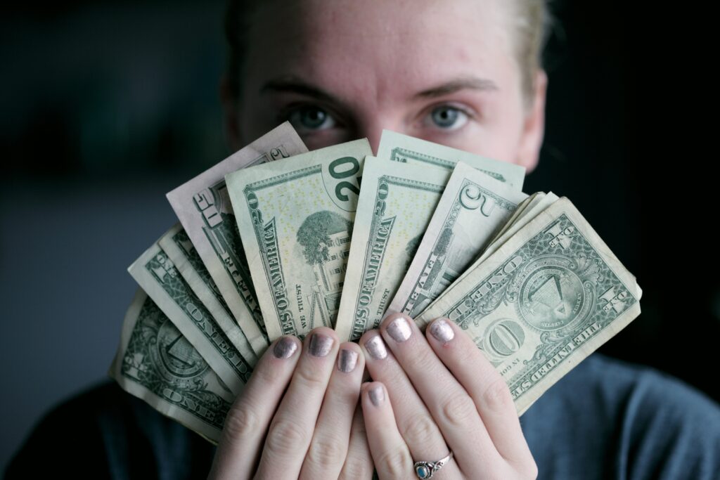 Photo of a woman with silver metallic nail paint covering her face with American currency bills signifying investment.